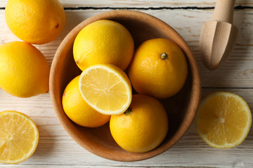 Bowl, lemons and wood juicer on wooden background, top view