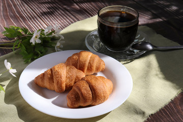 Breakfast outdoors on a bright sunny day. Fresh pastries, croissants, hot coffee and spring flowers on a wooden background.