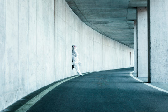 Man wearing protective clothing leaning against concrete wall in a tunnel