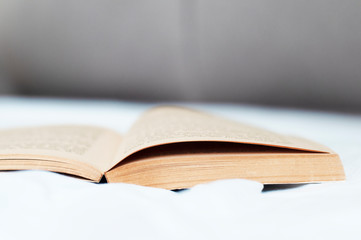Open book lying on bed. Old opened book on bed sheets. Bedtime reading, reading before bed or reading in bed concept. Low angle view.