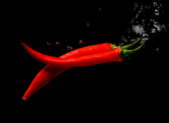 two pods of red chili peppers in water. Hot Peppers and bubbles of water on a black background