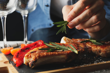 Person puts rosemary on steak. Composition with grilled food