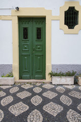 Portugal: Alte grüne Haustür und Fenster umrahmt von Natursteinen mit davor geometrisch verlegten...