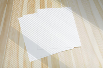 Blank poster flyer letterheads with window overlay shadow on light wooden desk as template for design presentation, event promotion, portfolio etc.