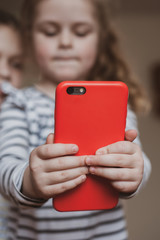 Two cute girls holding a red mobile phone in front of them.