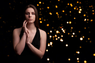 Teenage Girl with long hair and hands close to face in black top on black background with lights