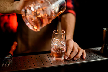 Close-up of barman accurate pouring drink into glass.