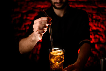 Close-up Barman's hand adds glassy drinking tube to glass with cocktail.