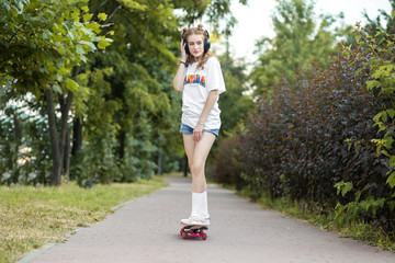 Teen girl rides on a skateboard. Listens to music on headphones. The concept of an hobby, music and sport.