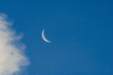 Obraz na płótnie Canvas A slim sliver of the silvery moon set on an expanse of a partly cloudy blue sky.