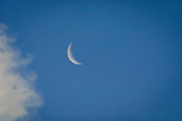 Naklejka na ściany i meble A slim sliver of the silvery moon set on an expanse of a partly cloudy blue sky.