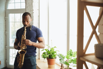 African-american musician playing saxophone during online concert at home isolated and quarantined....