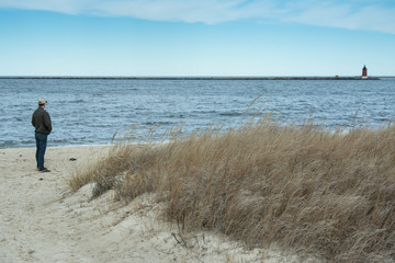 Single man looking out over water on bay beach at distant lighthouse on winter day © DanaDaglePhotography