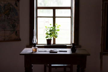 Old table with papers and a kerasin lamp by the window in a room with natural dim light. Vintage interior in an old house.
