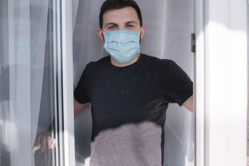 Fototapeta na wymiar Young man in protective mask at home open window to breathe fresh air. Coronavirus theme