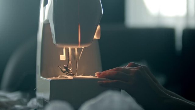 Hands of a young woman seamstress sewing a white cloth