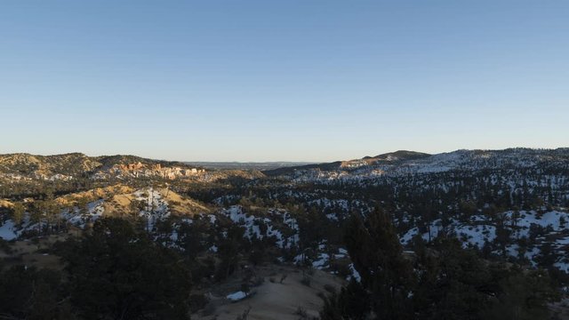 A wide sunset timelapse of red rocks and snow covered vegetation in Bryce Canyon National Park lighting up in stunning red colour as the sun moves towards the horizon.