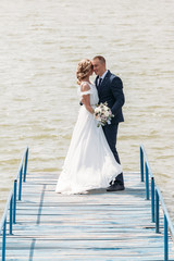 Fototapeta na wymiar bride and groom are in an embrace on the pier in the background of lake
