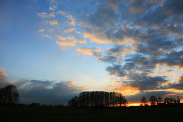 Kolorowy zachód słońca nad obszarem wiejskim, złote chmury i obłoki.