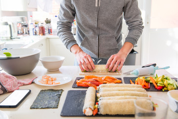 Cropped young caucasian man making sushi at home following cooking online video classes on website via smartphone. Internet technology for modern lifestyle concept. Soft selectove focus. Copy space.