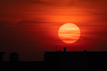 Scenery sun disk over dark building silhouette. Bloody sunrise
