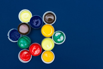 Top view of open acrylic paint cans. Colorful paints on blue background with copy space