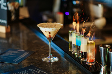 bar counter with fiery short cocktails. Creamy coffee cocktail in a martini glass. Flames in a glass. Burning cocktail
