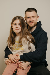 A young happy father with a beard hugs strongly his cute daughter. A girl with a smile sitting on daddy's lap. Family photo.

