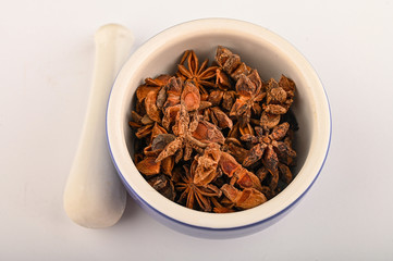 star anise in a blue ceramic spice mortar with a pestle on a white background. Close up.