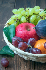 red grape berries and fresh fruits in a straw basket on a dark wooden background.