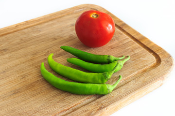 Tomato and green peppers on wooden chopping board at kitchen on isolated white background.