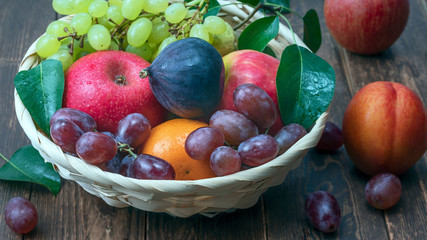 red grape berries and fresh fruits in a straw basket on a dark wooden background.