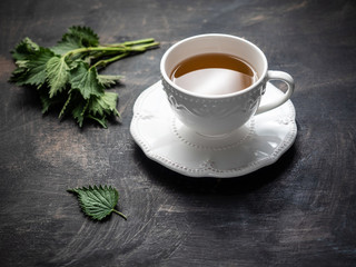 Fresh nettle tea in white ceramic cup on wooden vintage table.
