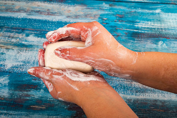 Fototapeta premium Someone is soaping their hands with a piece of toilet soap on a wooden background. Close up. Regular hand washing with soap is a prevention of COVID-19 infection.
