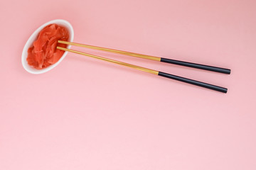 Marinated ginger and chopsticks with black handles, folded cross on a pink background. Flat lay with copy space, selective focus. Japanese food. Horizontal orientation.