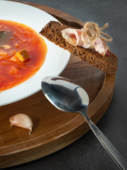 close up view to Red ukrainian borscht in white plate on wooden plate with dark bread and bacon on the dark background