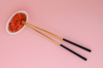Marinated ginger and chopsticks with black handles, folded cross on a pink background. Flat lay with copy space, selective focus. Japanese food. Horizontal orientation.