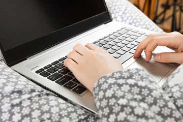 Front view on a screen of a laptop on the knees of a woman in a grey flowered nightwear. Home office concept. Freelancer works in a bed during outbreak of coronavirus
