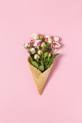 Small roses in waffle cone on pink background, copy space. Minimal style flat lay. For greeting card, invitation. March 8, February 14, birthday, Valentine's, Mother's, Women's day concept. Top view