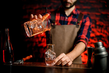 male bartender neatly pours cocktail from mixing cup into small glass.
