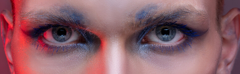 Big eyes of a young man with professional beauty makeup close-up. Banner panorama of blue eyelashes...