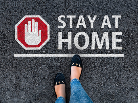 stay at home. woman with a shoes is standing next to line and word stay at home and hand stop sign on road asphalt. coronavirus self isolation concept