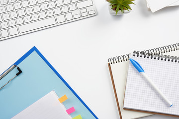 White wireless keyboard, a stack of notebooks, green plants in pots and a mouse, workplace of a freelancer