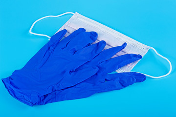 Protection concept - pair of latex medical gloves and surgical mask on a blue background.