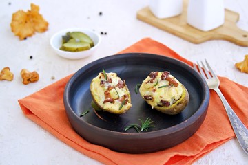 Twice baked potatoes with cheese and chanterelle mushrooms on a brown clay plate on a light concrete background. Recipes with potatoes. Cooking wild mushrooms.