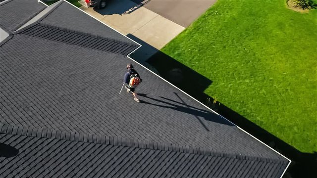 Man cleaning leaves and debris from the roof of a modern suburban home with a backpack style leaf blower.