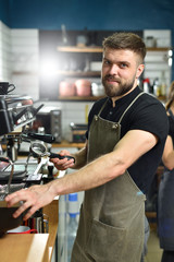 A young barista guy makes coffee on a large professional coffee machine. Small business and work concept for young people