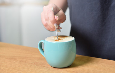 Barista bartender creates a drawing on the surface in a cup of coffee, close-up.