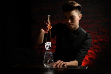 bartender accurate hold tweezers with large piece of ice over glass