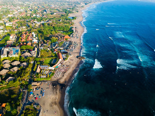 Tropical blue ocean with waves and coast with beach, green palms, villas and hotels. Top view aerial drone exotic landscape, Bali, Indonesia.